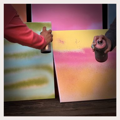 OOYAH-Graffiti-Workshop. Hände vor besprühten Leinwänden