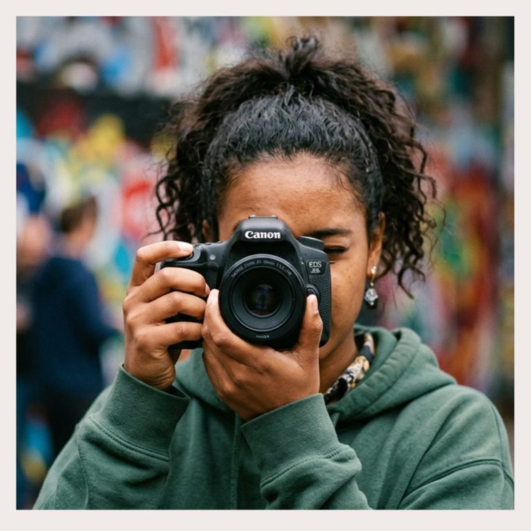 OOYAH-Creative Recap.Junge Person mit einer Kamera in der Hand, vor einer bunten Graffiti-Wand.
